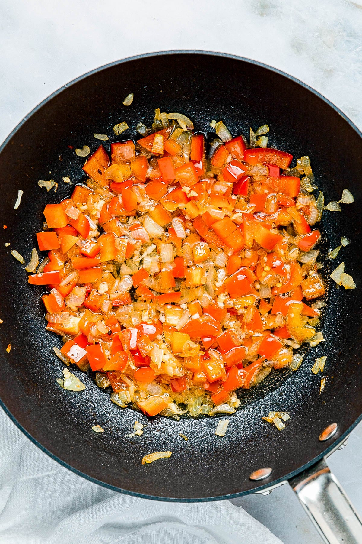 Diced red bell peppers and onions cooking in a black frying pan.