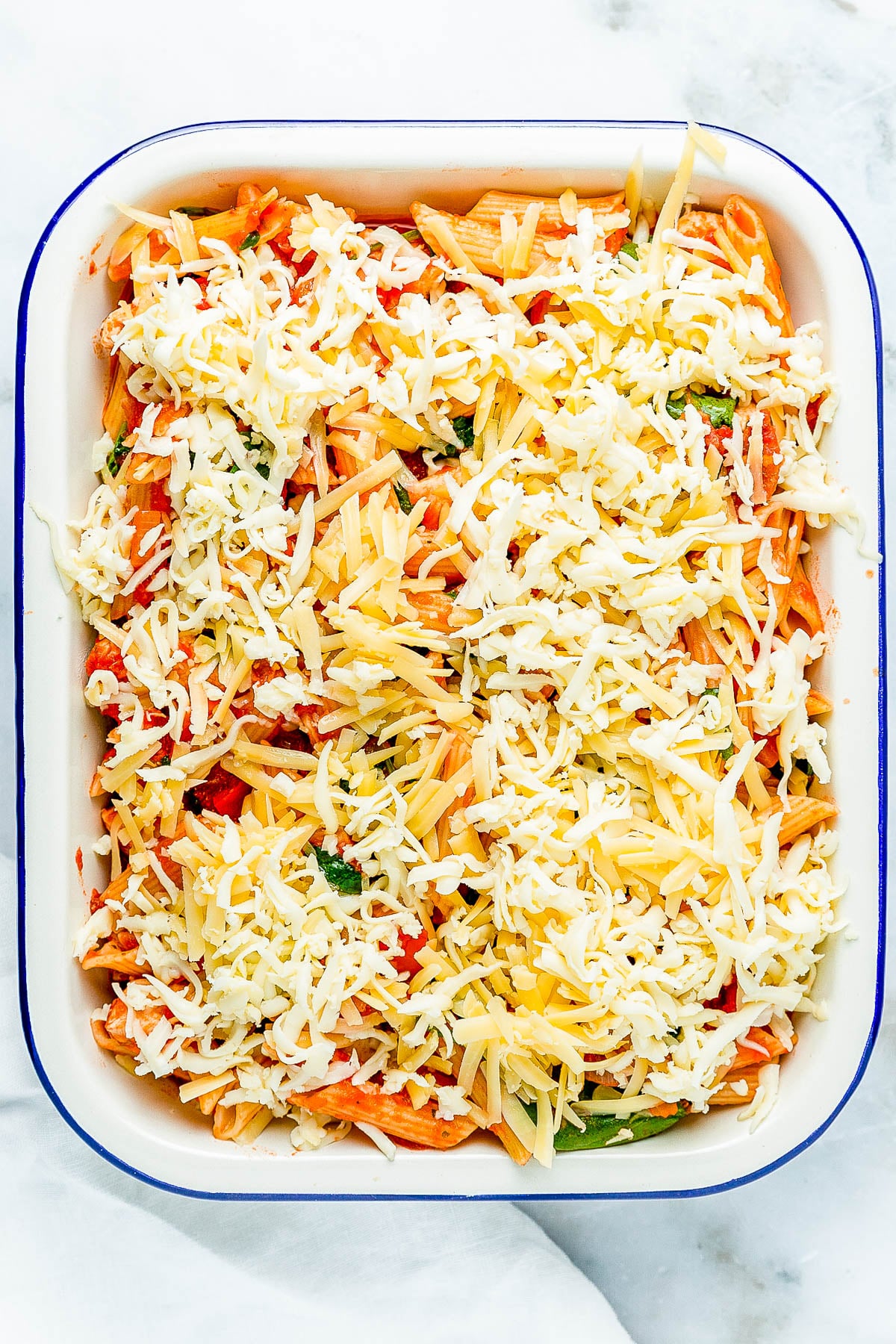 A baking dish filled with penne pasta, bell peppers, and shredded cheese, ready for baking.