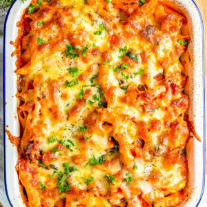 Baked pasta dish with melted cheese and parsley served in a white rectangular dish on a wooden surface.