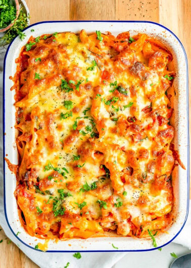 Baked pasta dish with melted cheese and parsley served in a white rectangular dish on a wooden surface.