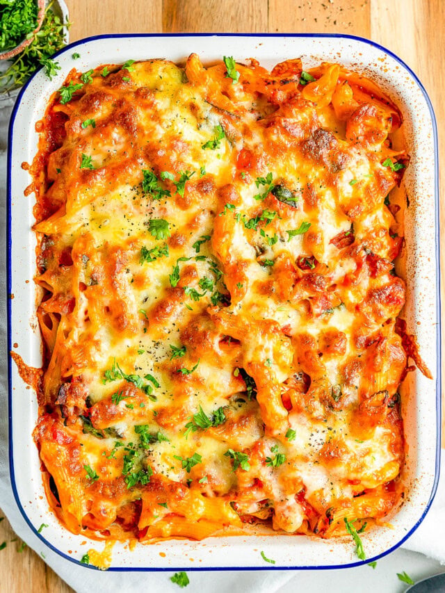 Baked pasta dish with melted cheese and parsley served in a white rectangular dish on a wooden surface.
