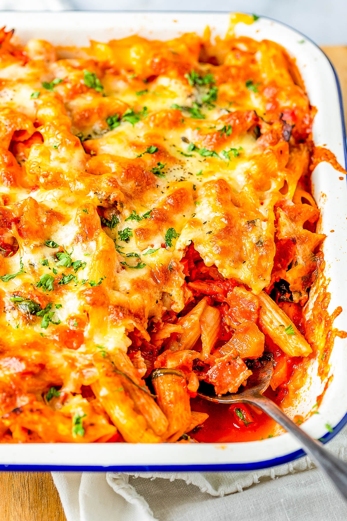 Baked pasta dish with melted cheese and herbs, partially served in a white dish on a wooden surface.