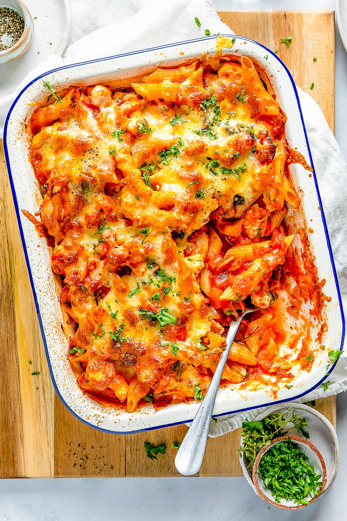 Baked cheesy pasta in a rectangular dish, garnished with herbs, with a serving spoon.