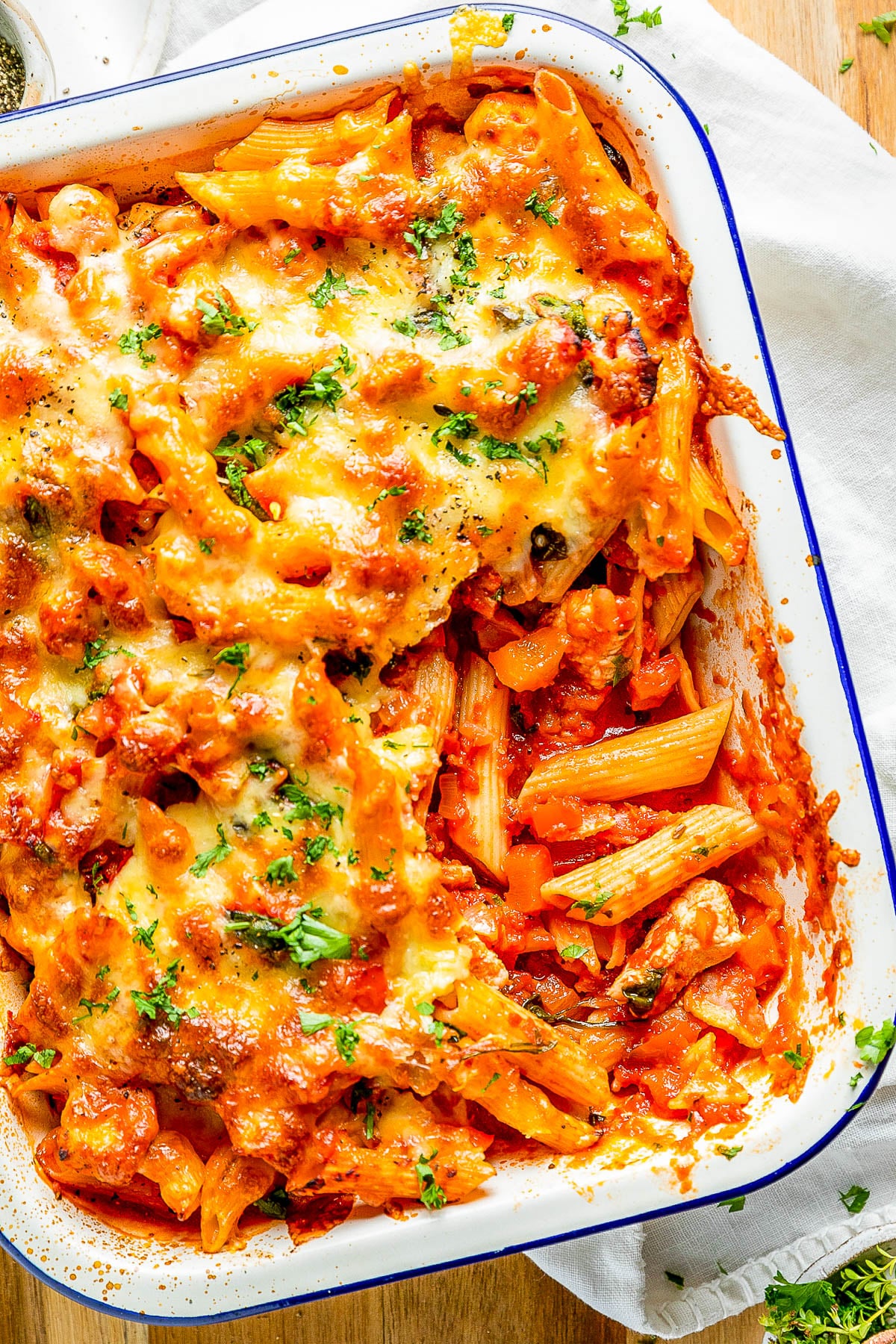 Baked pasta in a dish with melted cheese, tomato sauce, and herbs on top.