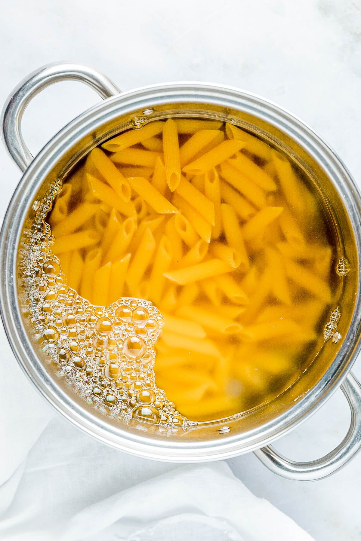 Pot of penne pasta boiling in water with bubbles forming on the surface.