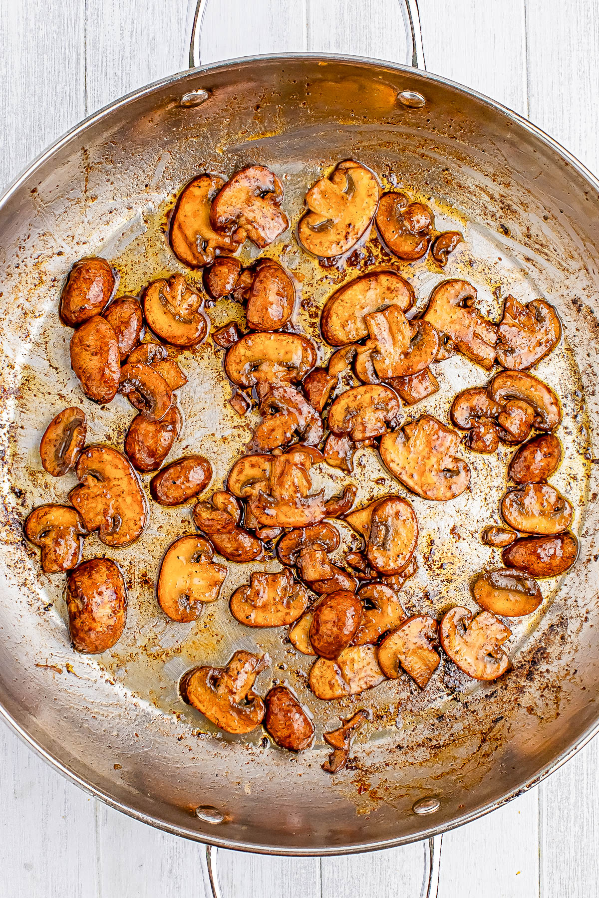 Saut&eacute;ed mushrooms in a large silver skillet on a light wooden surface.