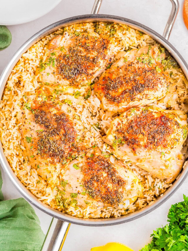 A skillet with seasoned chicken thighs on a bed of cooked rice, garnished with herbs.