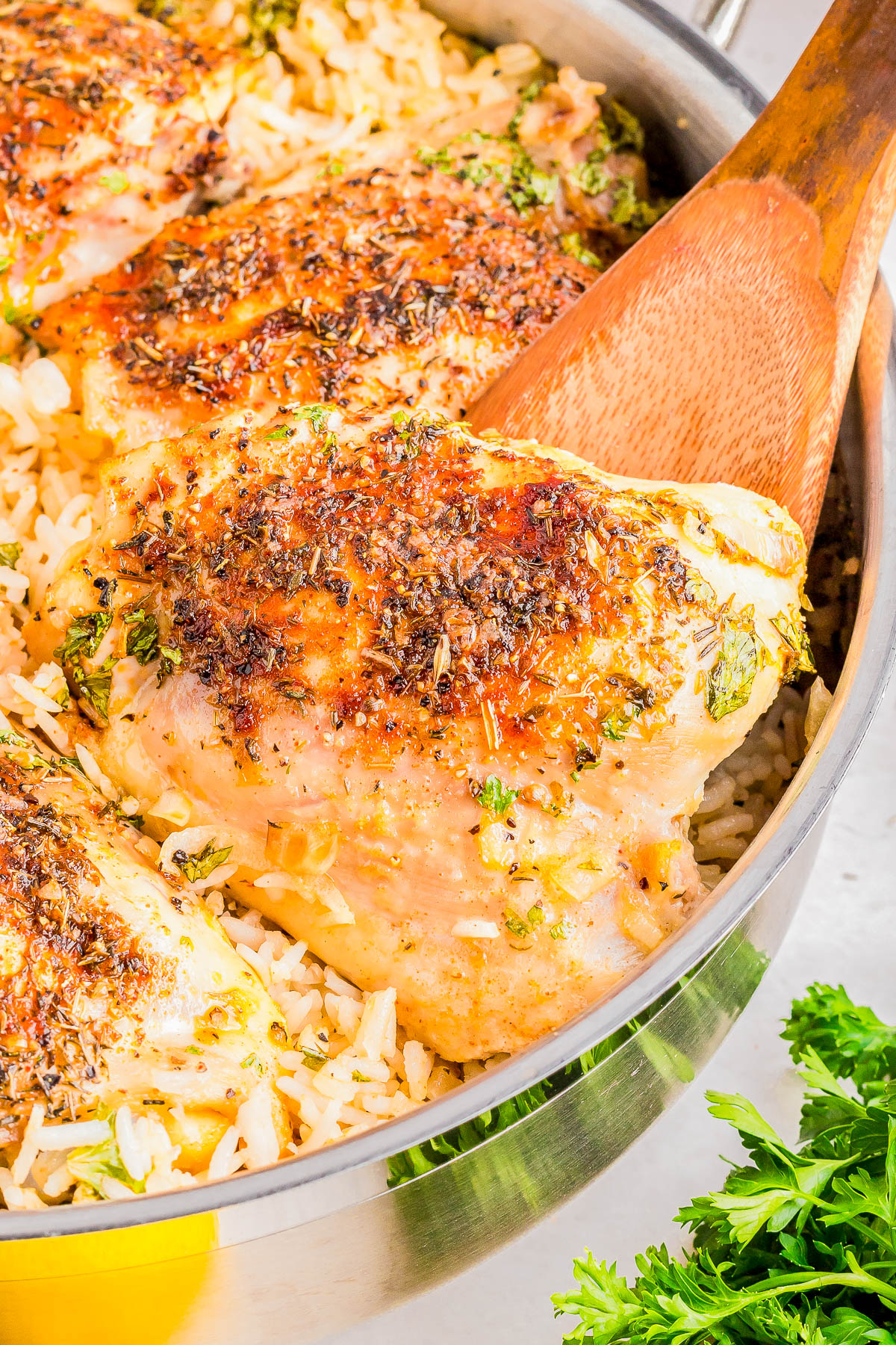 Chicken thighs seasoned and baked over rice in a skillet. A wooden spoon rests next to the chicken. Parsley garnish visible.