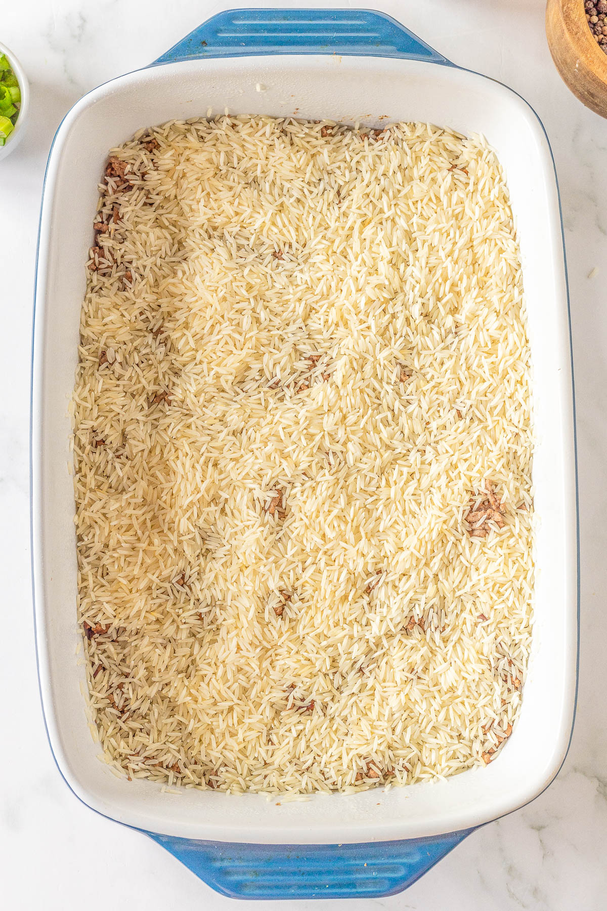 A blue rectangular baking dish filled with uncooked rice placed on a white marble surface.