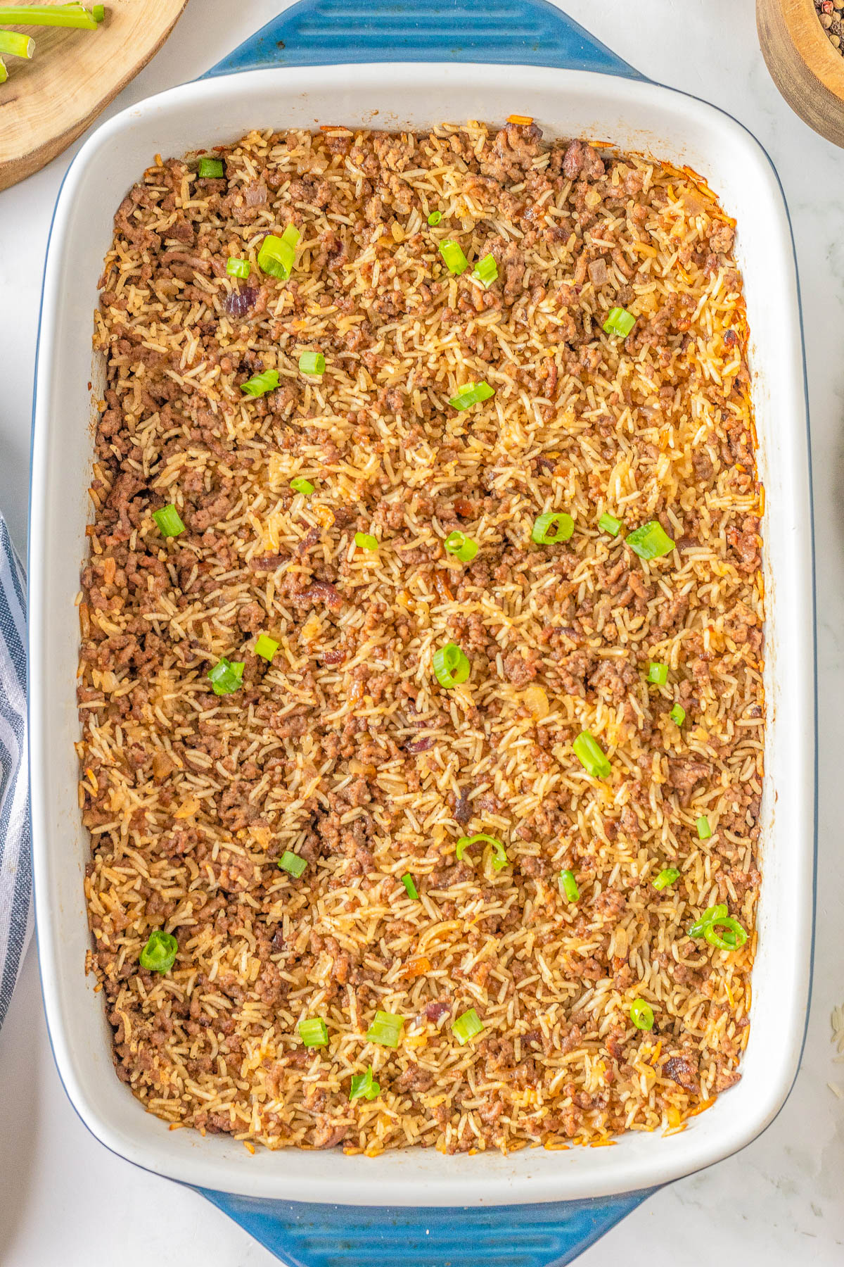 Baked casserole dish filled with seasoned rice garnished with chopped green onions in a blue rectangular baking pan.