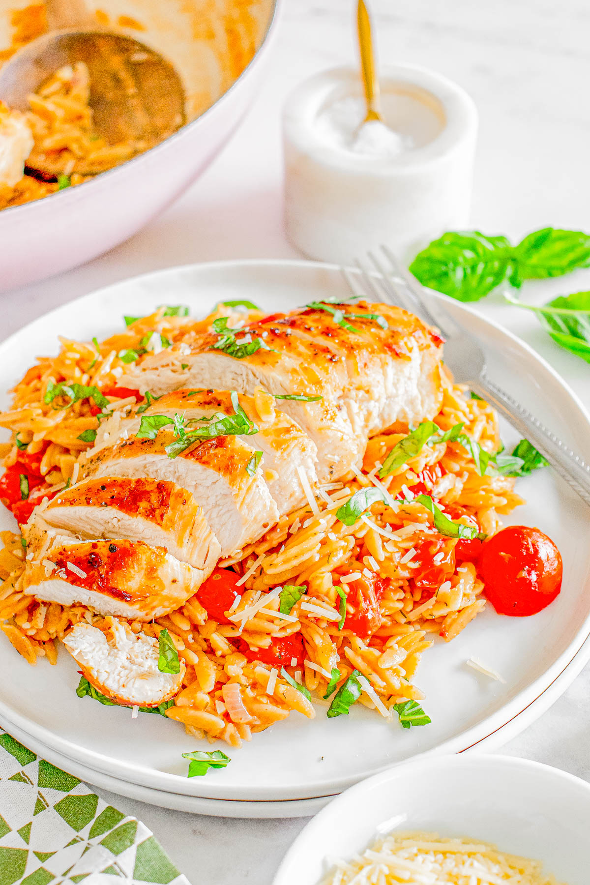 Sliced grilled chicken served over orzo pasta with tomatoes and herbs on a white plate, garnished with cheese.