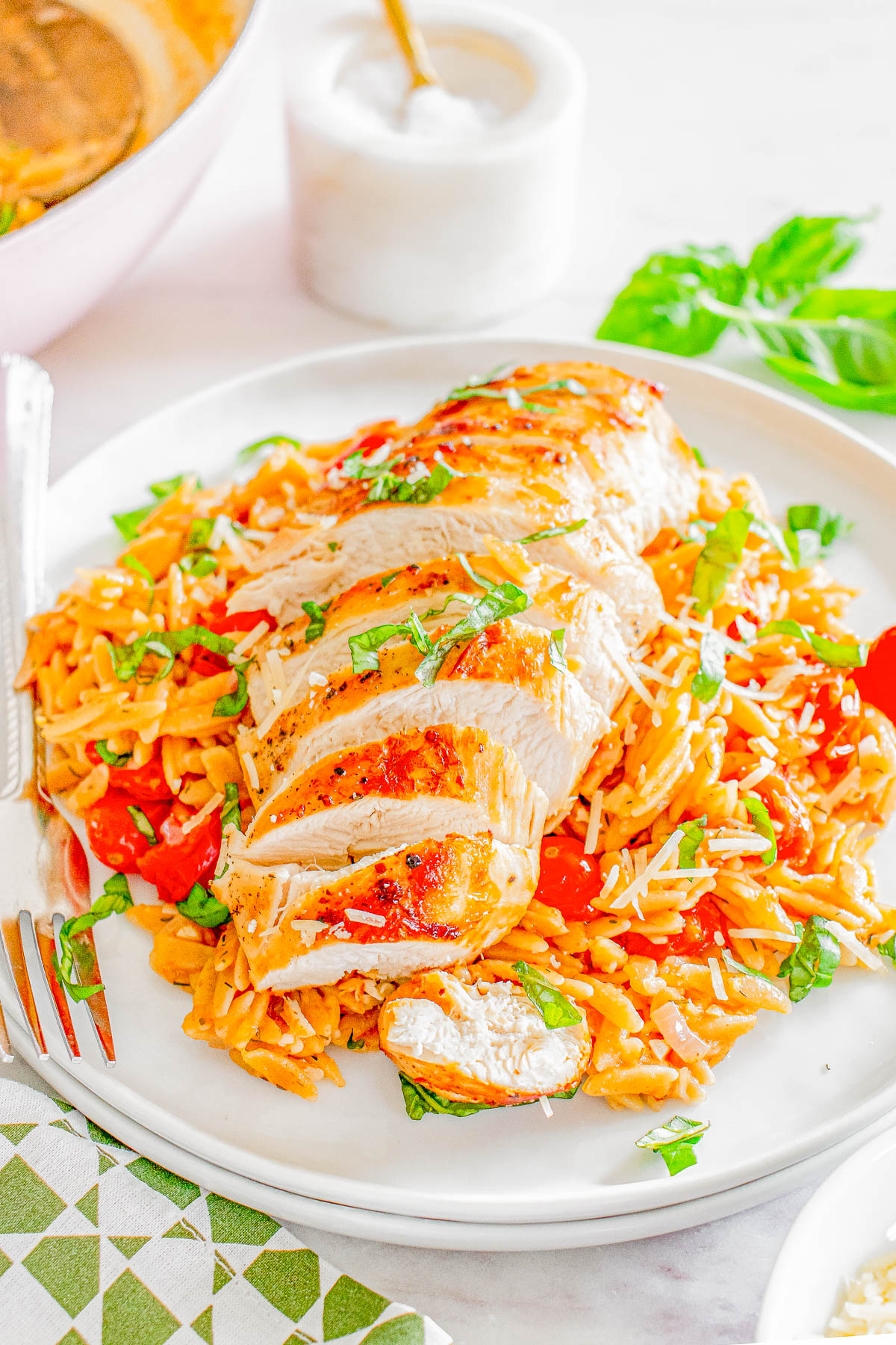 A plate of sliced grilled chicken breast on a bed of orzo pasta mixed with tomatoes and herbs.