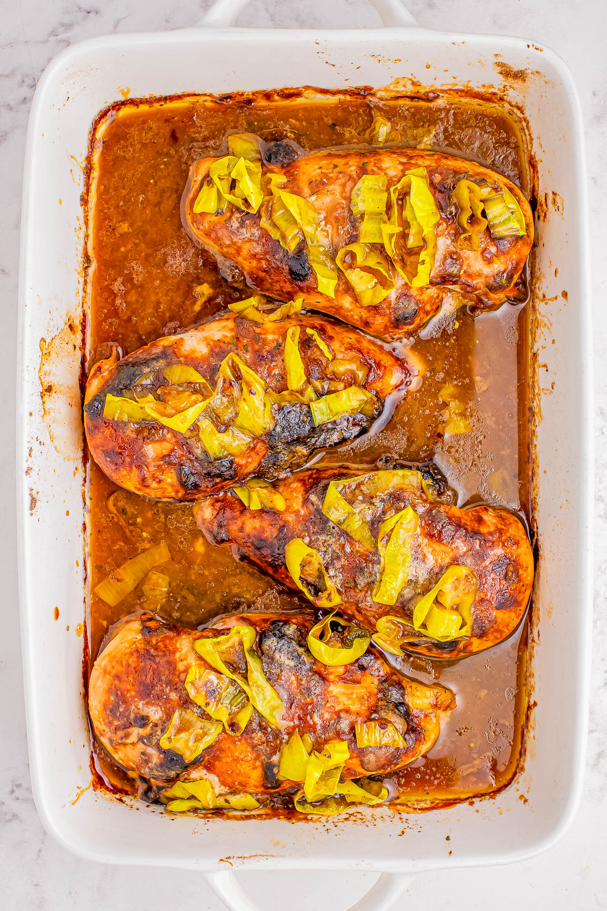 Baked chicken breasts in a rectangular dish, topped with a sauce and sliced green peppers.