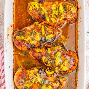 Baked chicken breasts topped with brown sauce and sliced yellow peppers in a white baking dish.
