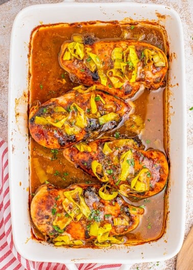 Baked chicken breasts topped with brown sauce and sliced yellow peppers in a white baking dish.