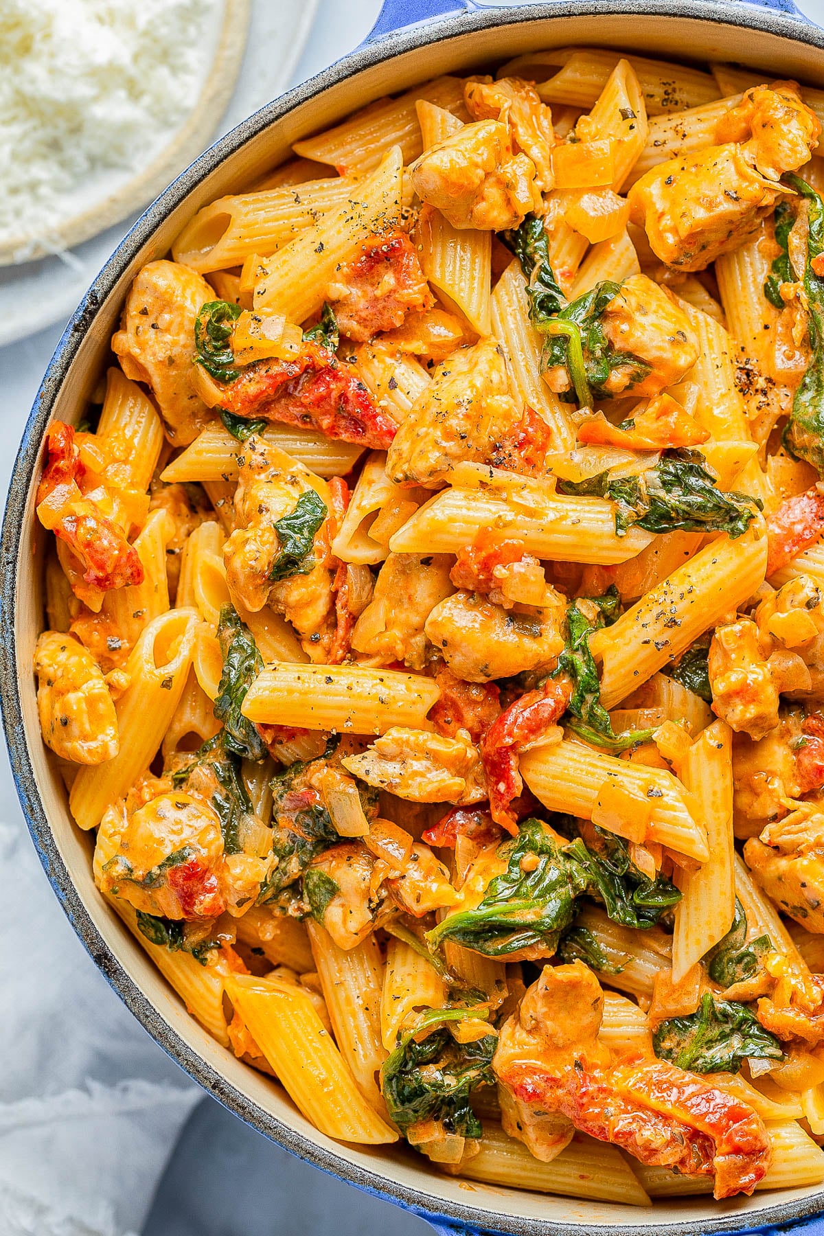 A pot of creamy penne pasta with chicken, sun-dried tomatoes, and spinach in a cheesy, tomato-based sauce.