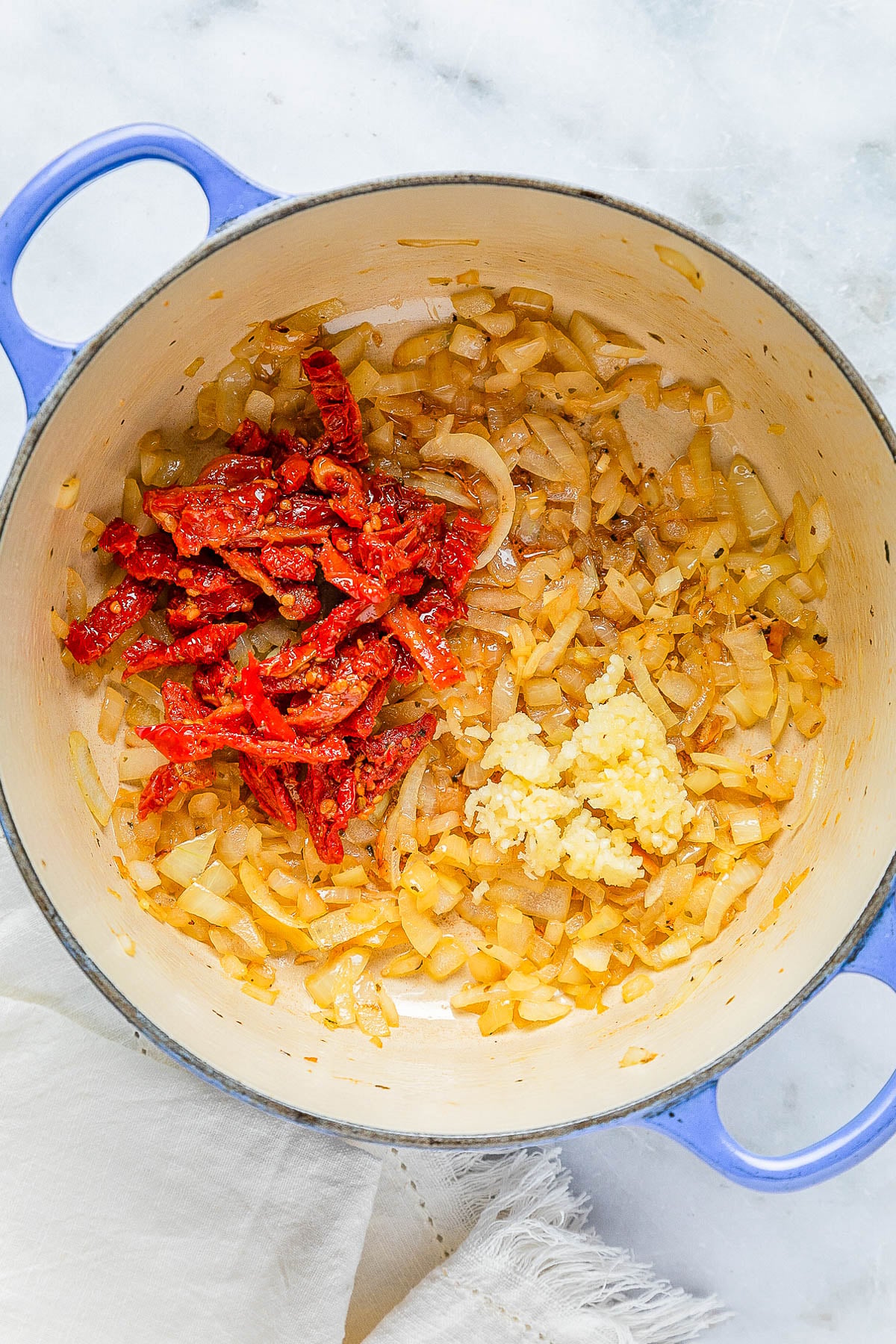 Diced onions, chopped sun-dried tomatoes, and minced garlic in a blue pot.