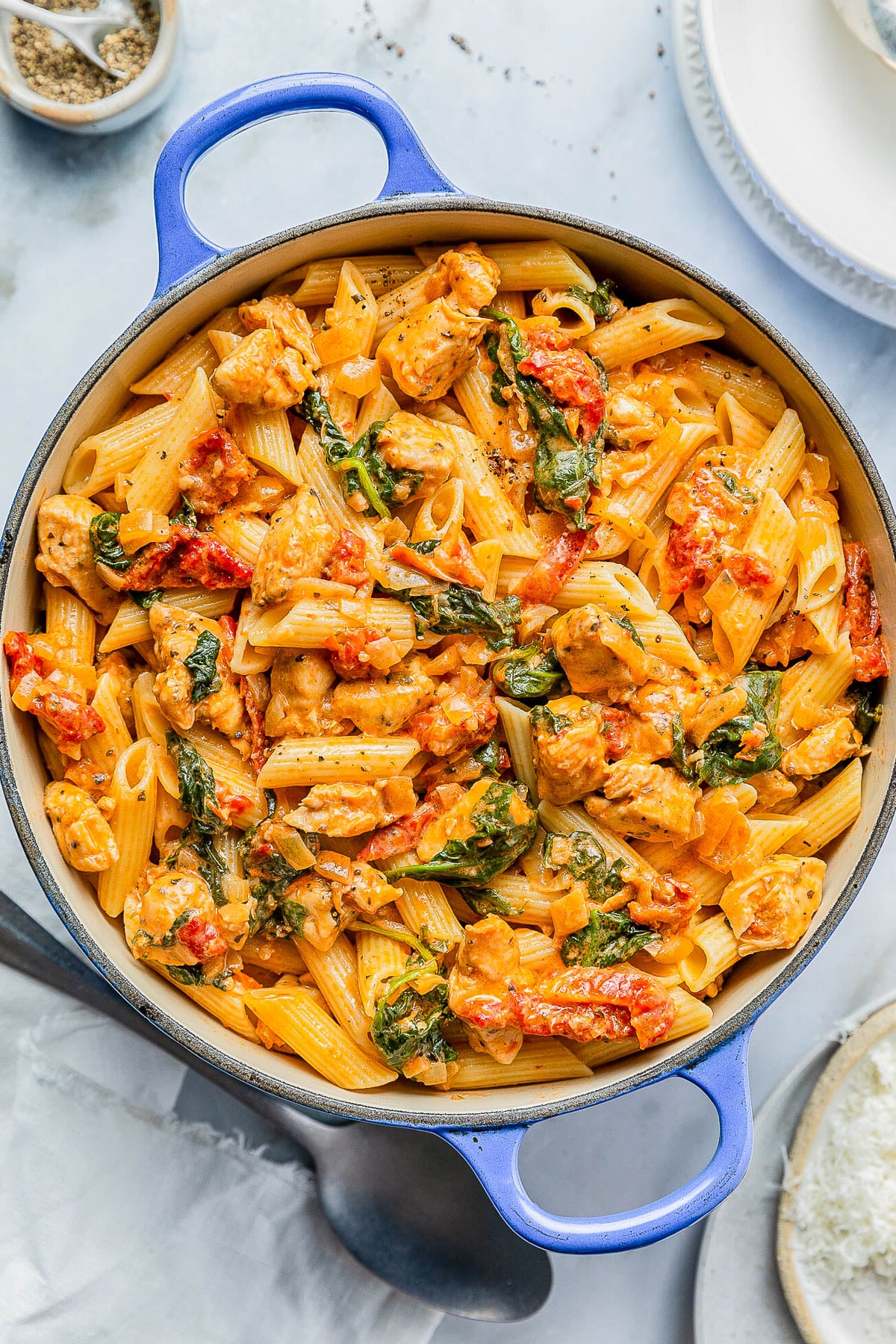 A pot filled with cooked penne pasta mixed with pieces of chicken, spinach, and a tomato-based sauce.