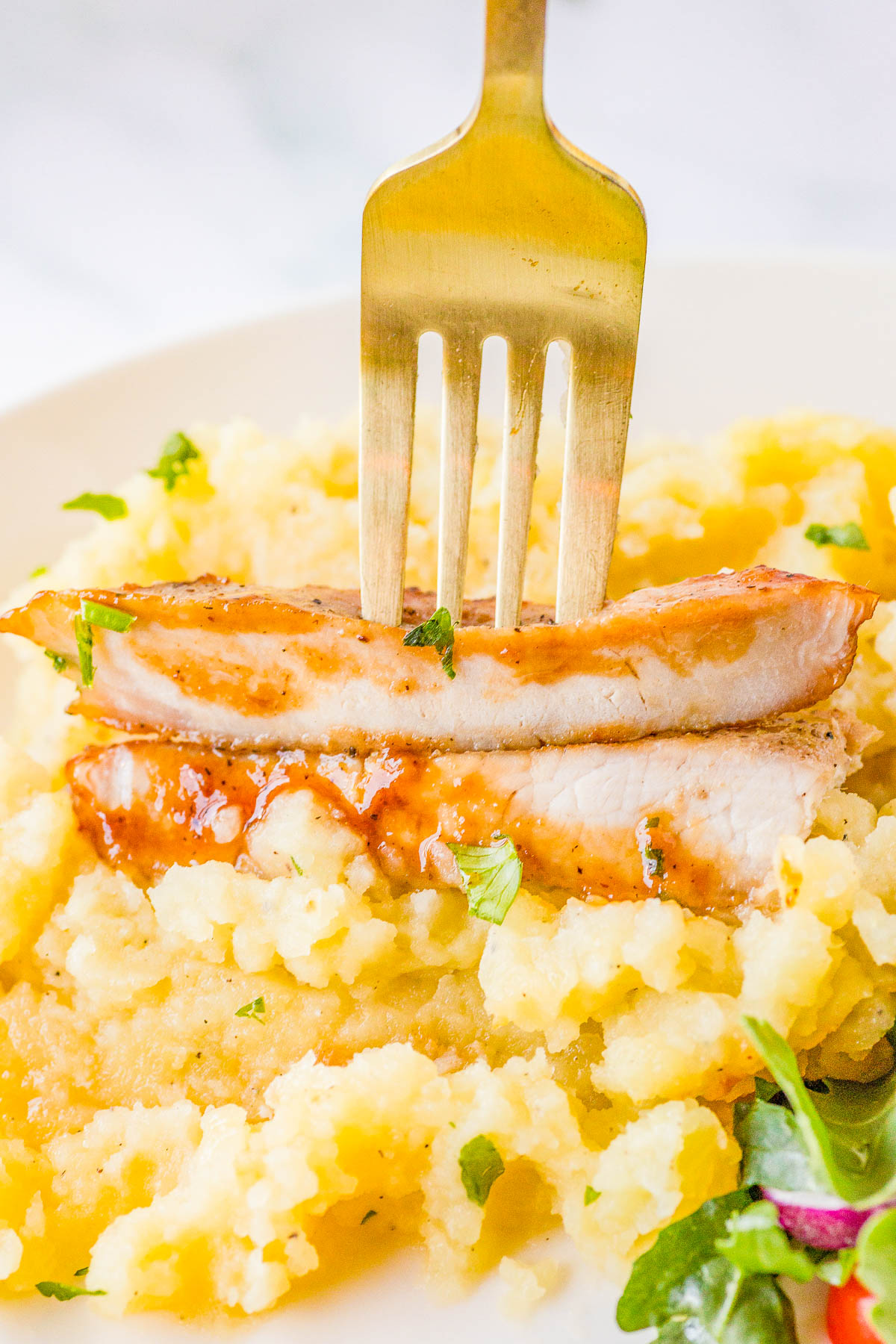 A fork spears a slice of grilled chicken breast atop mashed potatoes, garnished with herbs.