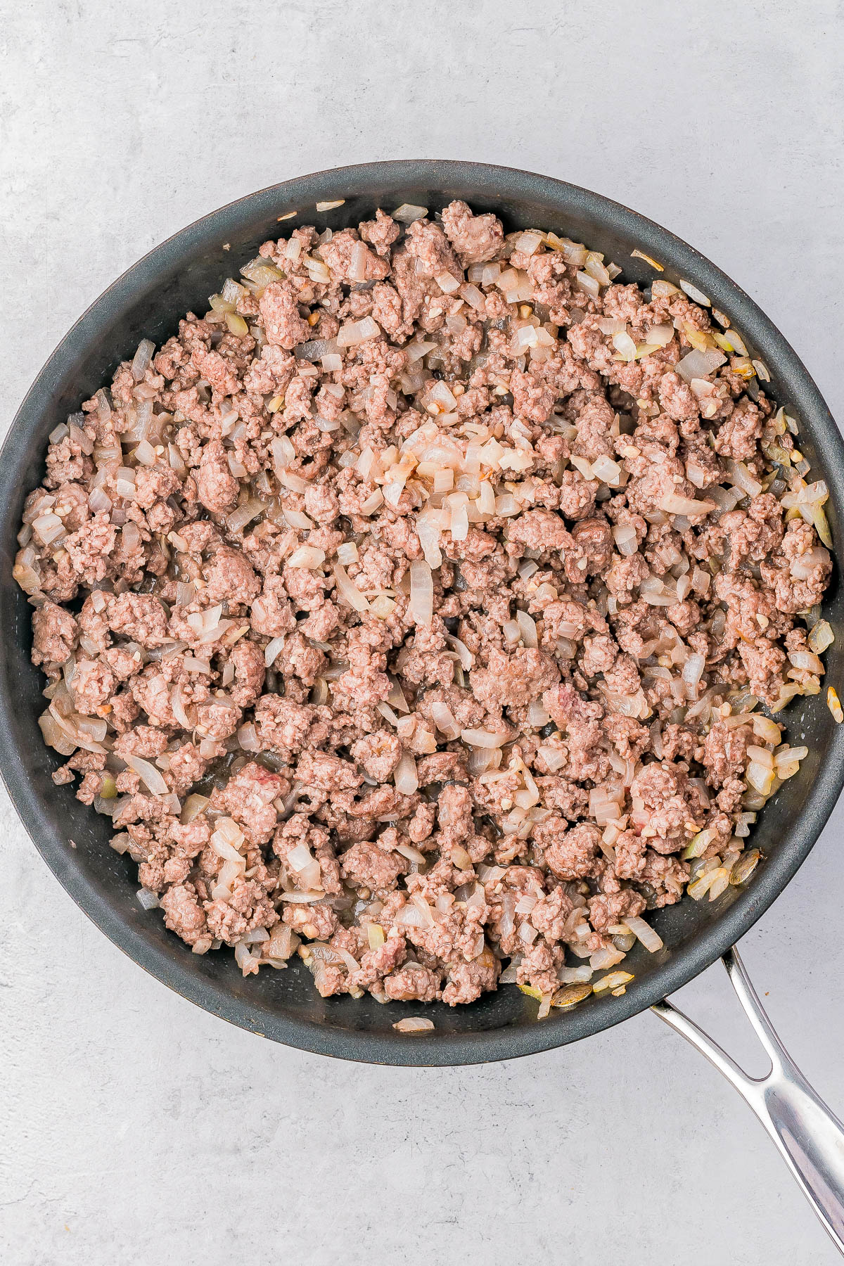 A frying pan filled with browned ground meat and diced onions.