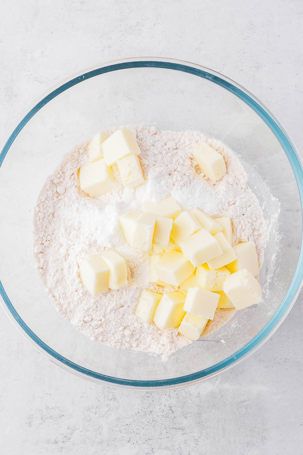 Cubed butter on top of flour in a clear glass bowl.