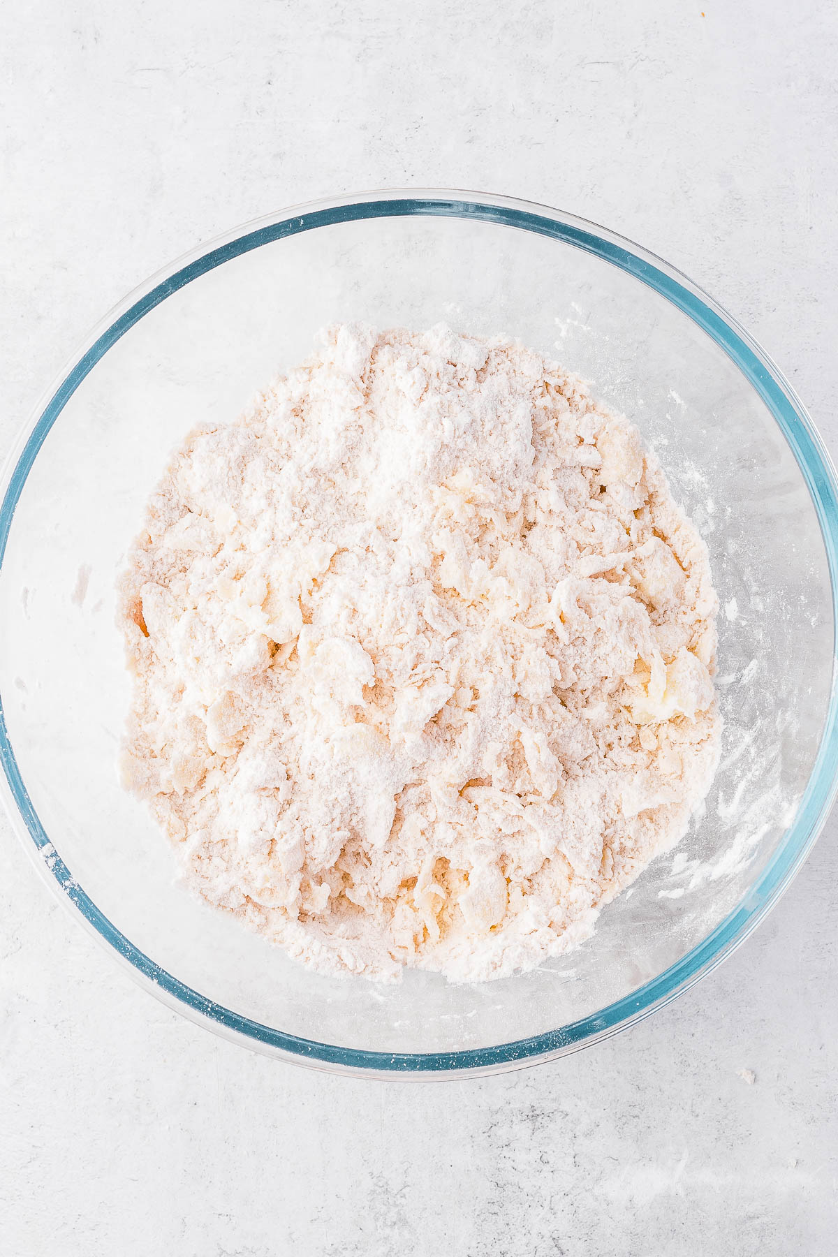 A glass bowl filled with a mixture of flour and butter on a light surface.