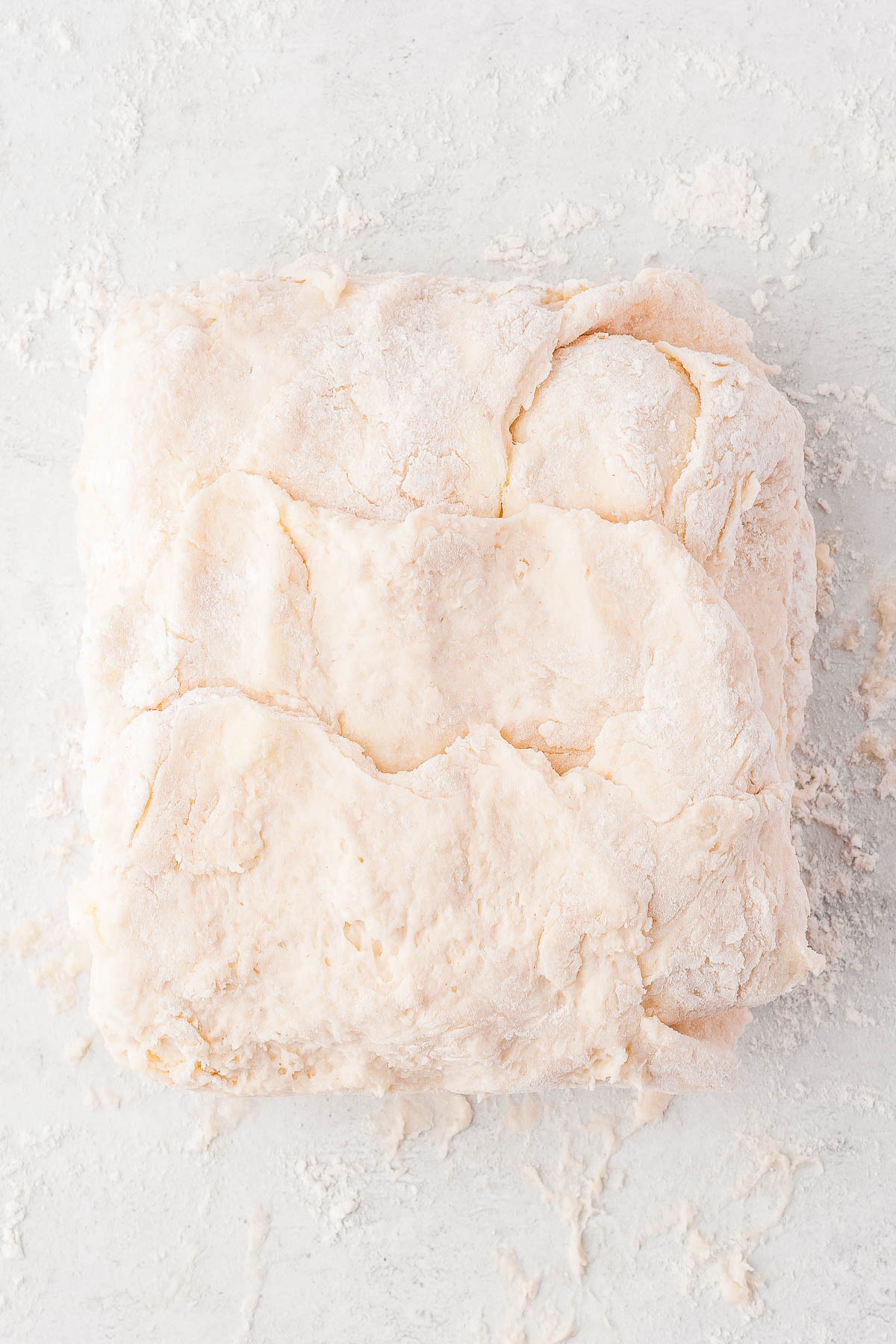 A square lump of dough on a floured surface, showing a layered texture.