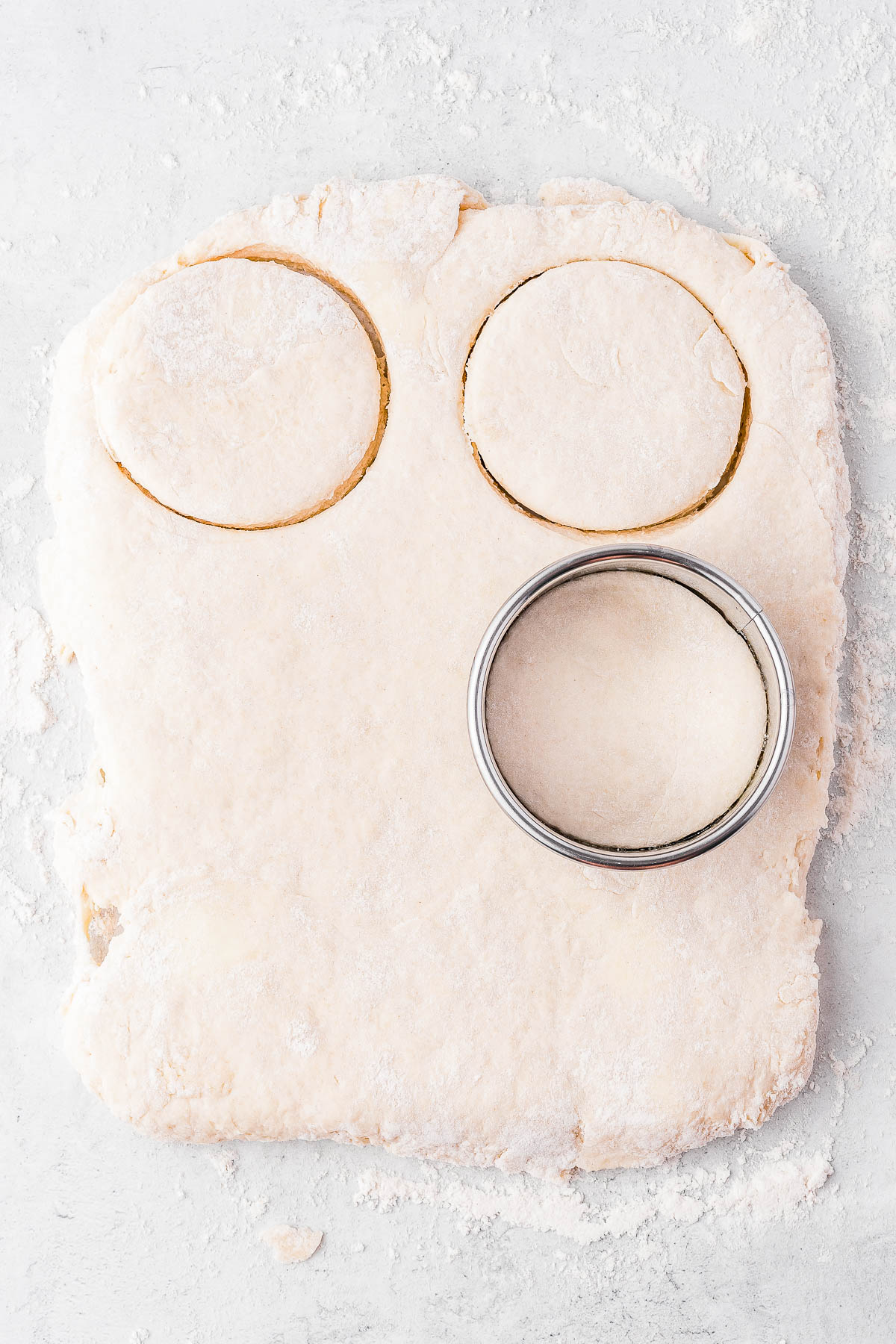 Dough on a floured surface with two cut-out circles and a round cutter.