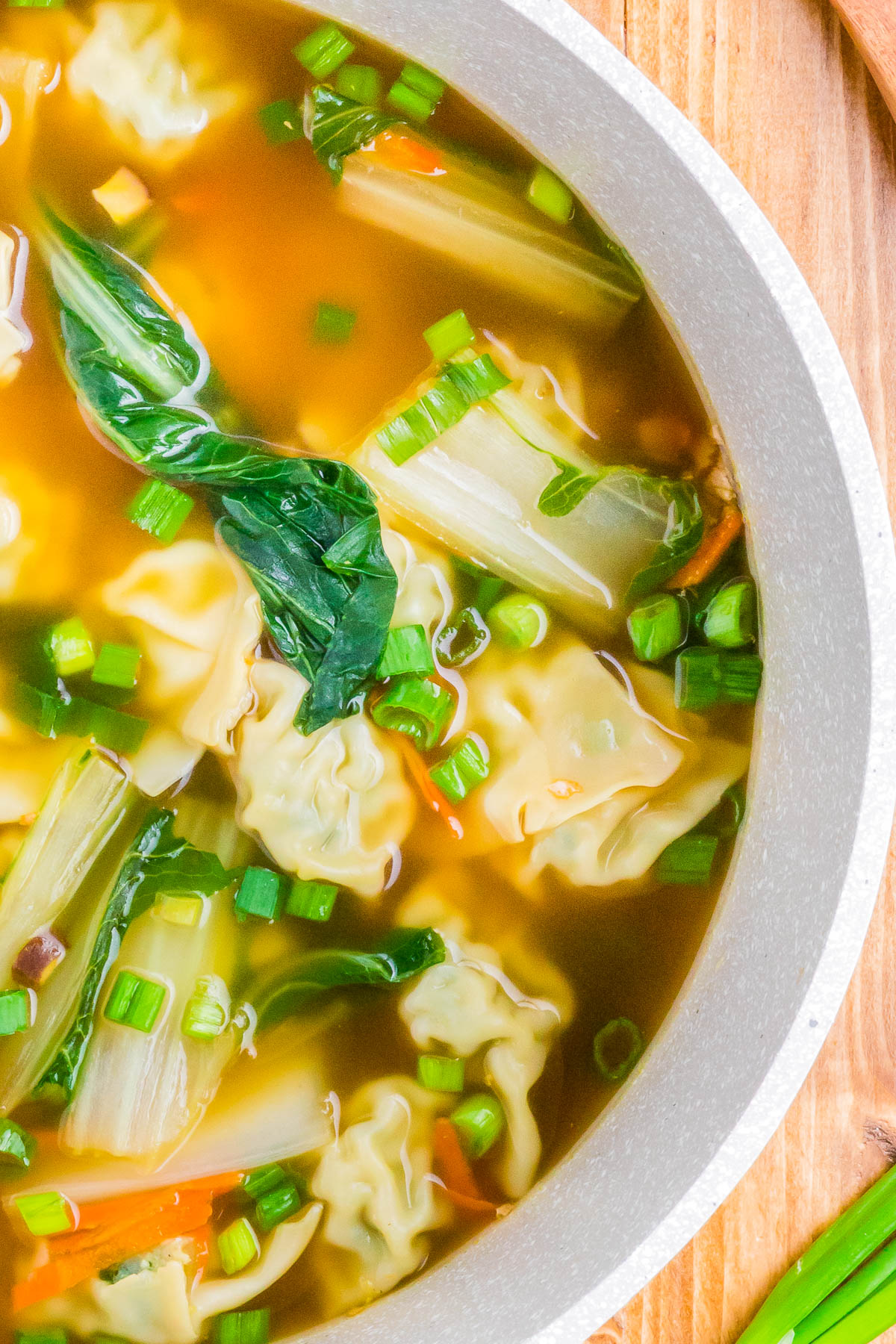 A bowl of dumpling soup with green onions and greens in a clear broth.