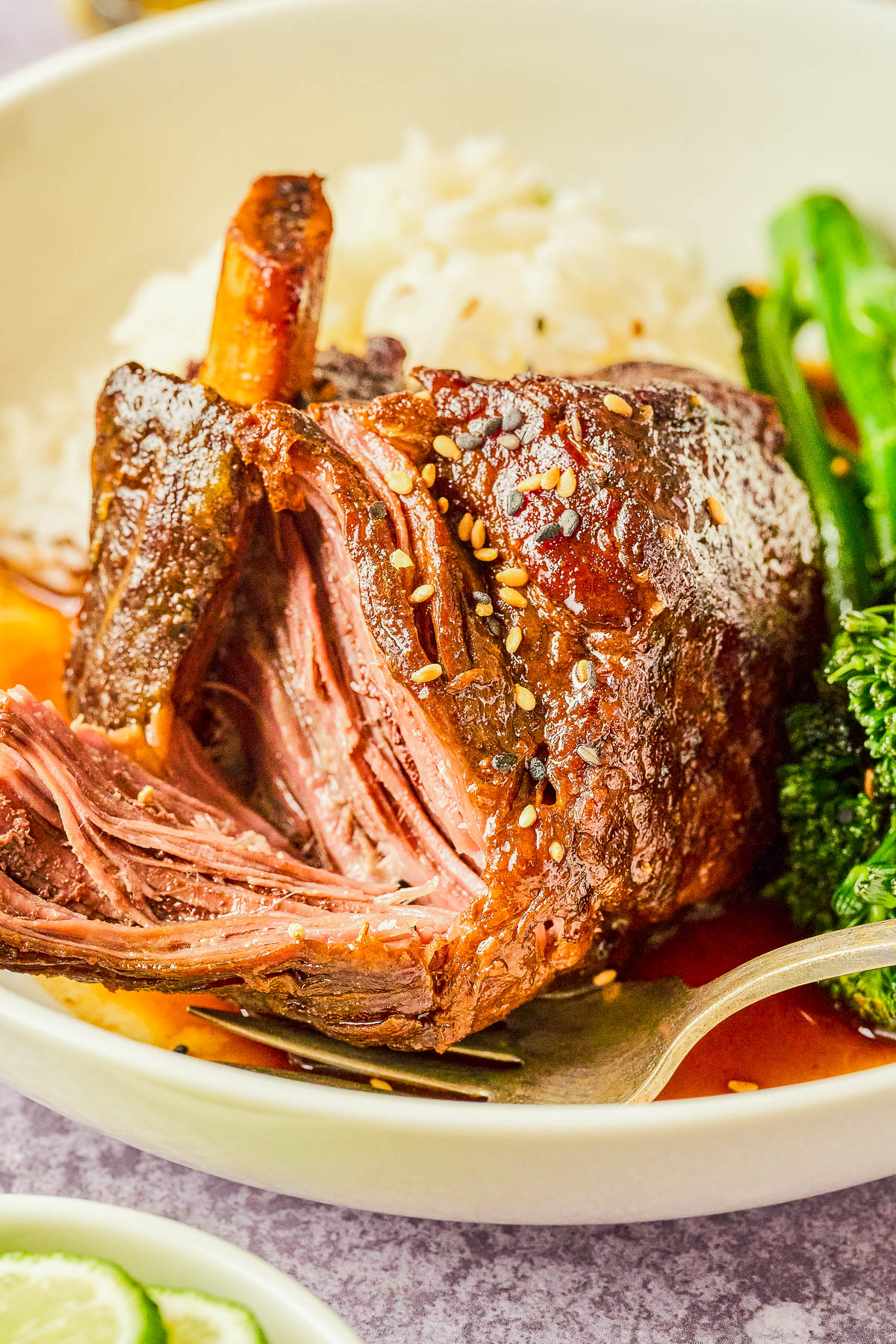A plate with tender, shredded beef garnished with sesame seeds, accompanied by rice and green vegetables, with a fork resting beside the beef.