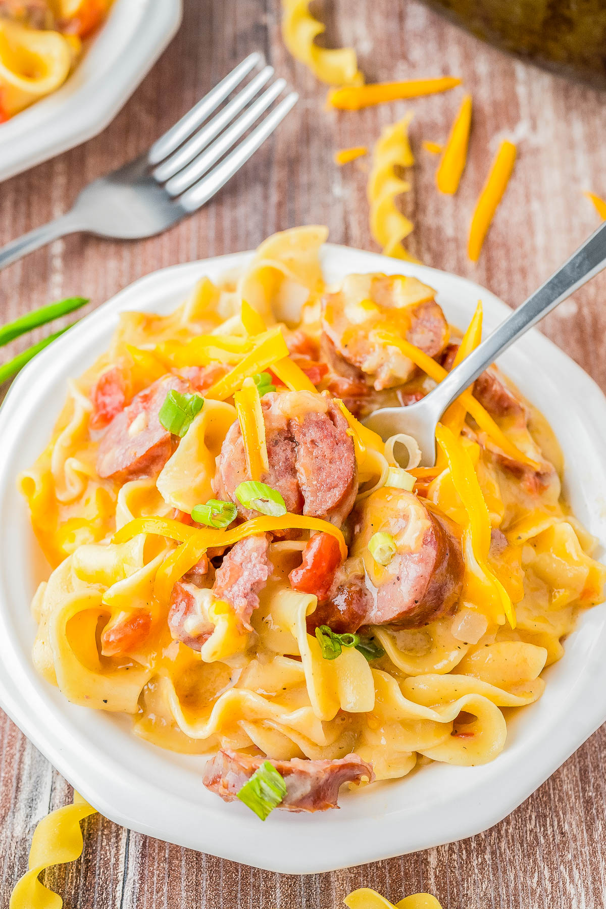 A plate of creamy pasta with sliced sausage, bell peppers, shredded cheese, and green onions, served with a fork.