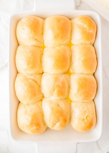 A baking dish containing twelve golden brown dinner rolls arranged in a 3x4 grid, resting on a light surface.