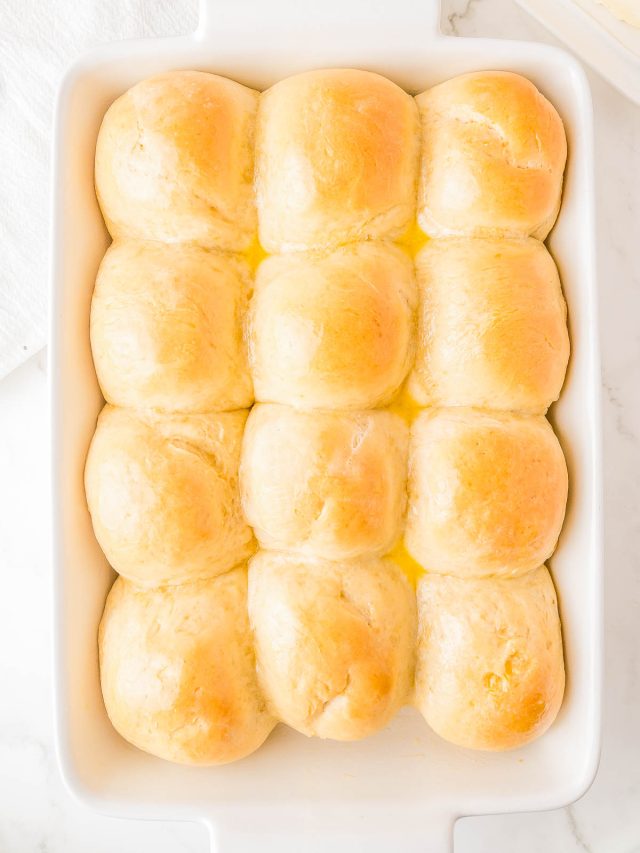 A baking dish containing twelve golden brown dinner rolls arranged in a 3x4 grid, resting on a light surface.