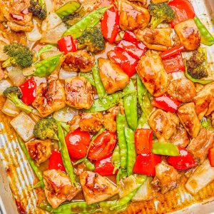Sheet pan dish with glazed chicken pieces, red bell peppers, broccoli, snow peas, and onions.