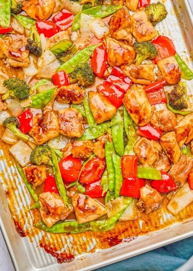 Sheet pan dish with glazed chicken pieces, red bell peppers, broccoli, snow peas, and onions.