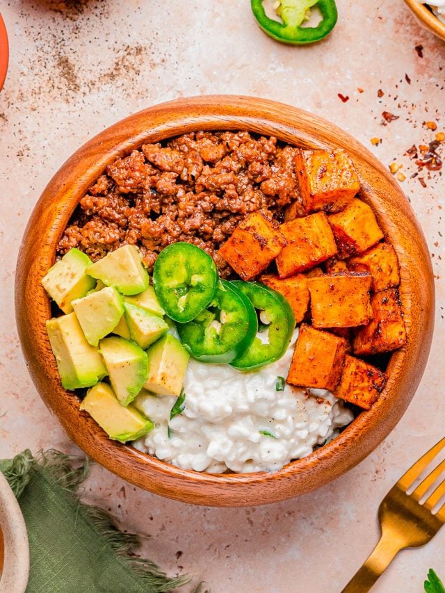 A wooden bowl containing seasoned ground meat, roasted sweet potatoes, diced avocado, cottage cheese, and sliced jalapeño, arranged in sections.