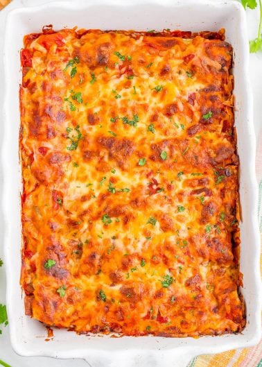 A baked casserole dish filled with golden-brown, cheesy lasagna topped with chopped herbs.