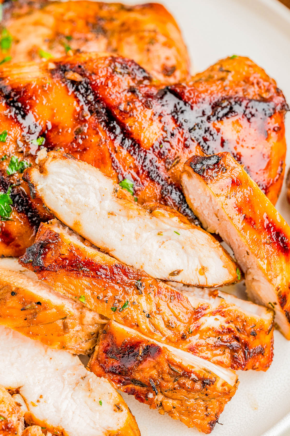 Close-up of grilled, sliced chicken breast with a golden-brown, slightly charred exterior, served on a white plate.