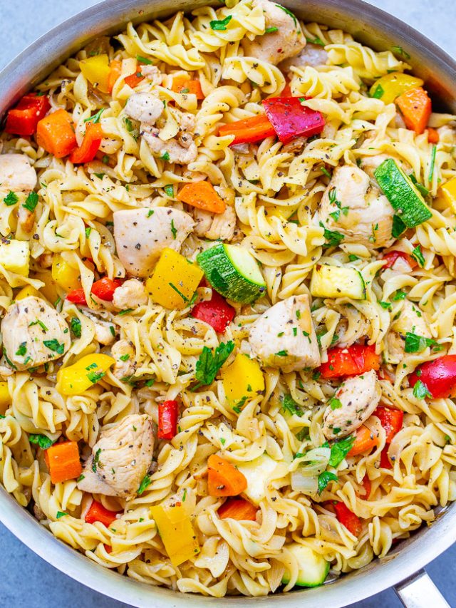 A skillet filled with rotini pasta, diced chicken, and mixed vegetables including zucchini, bell peppers, and carrots, garnished with chopped herbs.