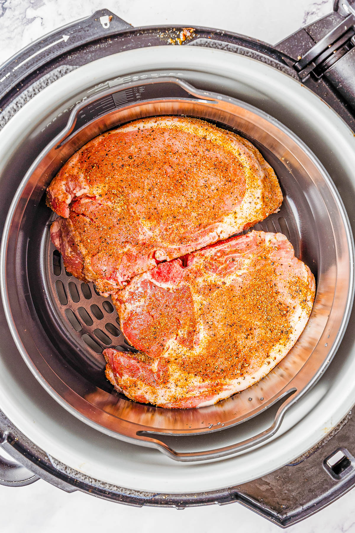 Two seasoned pork steaks placed inside an air fryer basket, ready to be cooked.