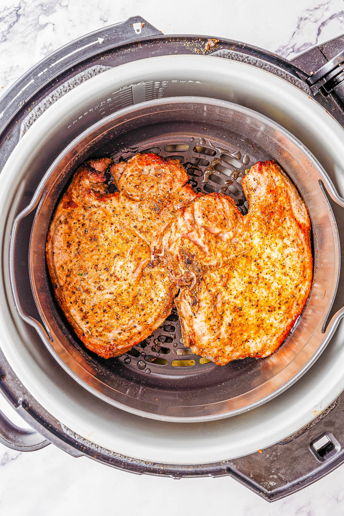 Two seasoned pork chops cooked in an air fryer basket, viewed from above.