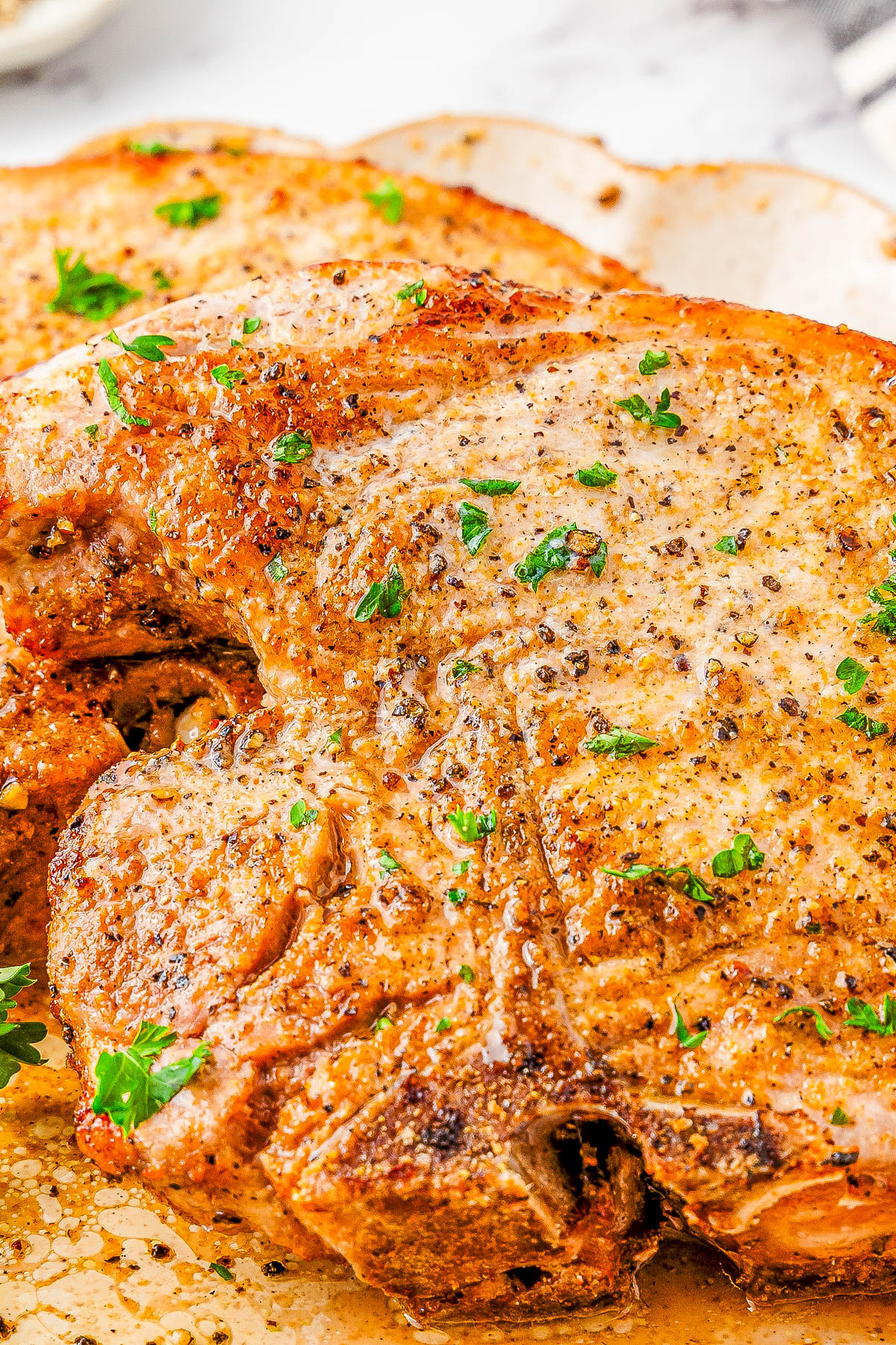 Close-up of seasoned, cooked pork chops garnished with chopped parsley on a white plate.
