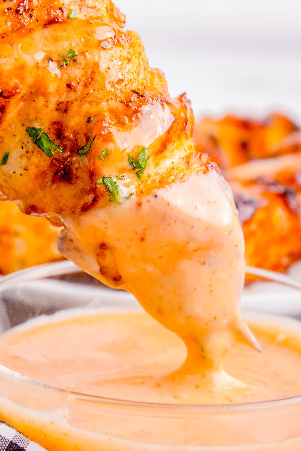 A grilled chicken skewer is dipped into a creamy orange sauce in a clear glass bowl.