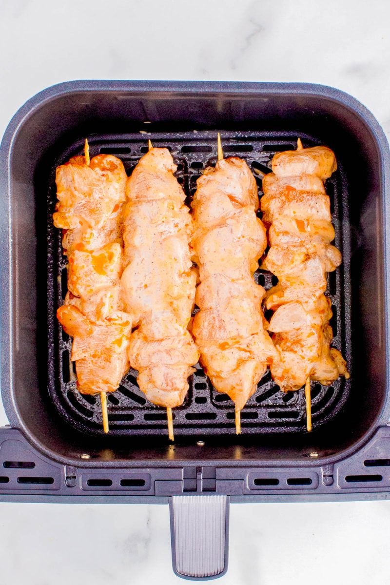 Four raw chicken skewers placed inside an air fryer basket, ready to be cooked.