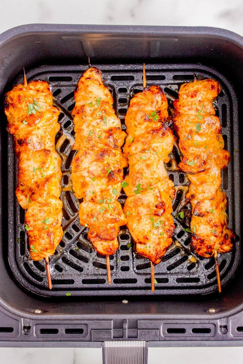 Four cooked chicken skewers are arranged side by side inside an air fryer basket.