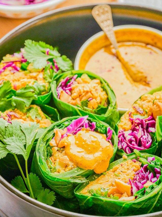 Collard green wraps filled with vegetables and rice, garnished with cilantro and purple cabbage, served with a bowl of creamy yellow dipping sauce.