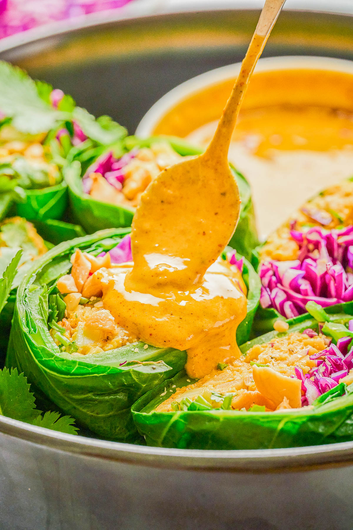 A spoon drizzles creamy orange sauce over vegetable wraps filled with greens, shredded cabbage, and chopped peanuts.