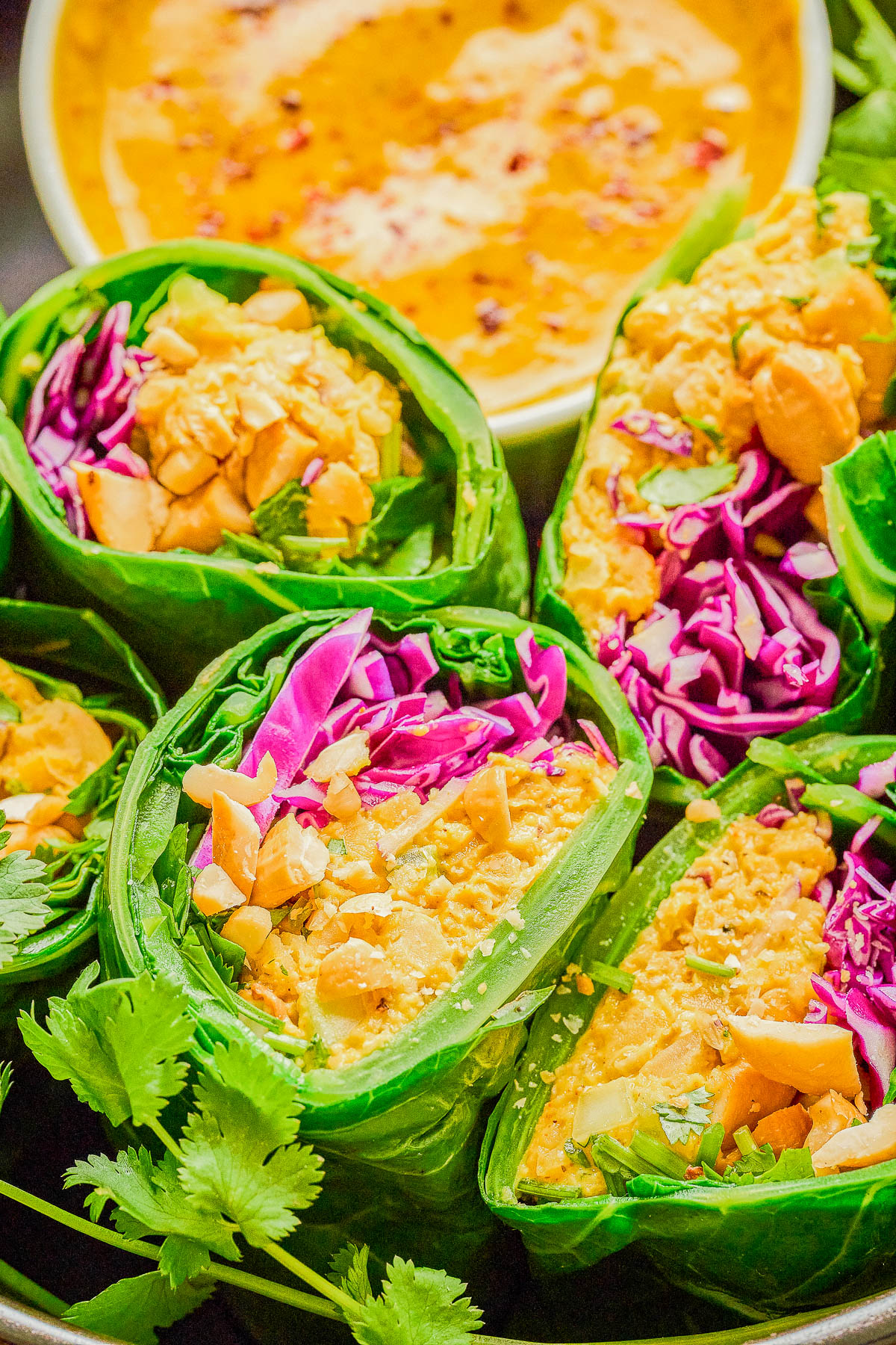 Fresh vegetable wraps filled with greens, purple cabbage, crushed peanuts, and served with a creamy dipping sauce in the background.