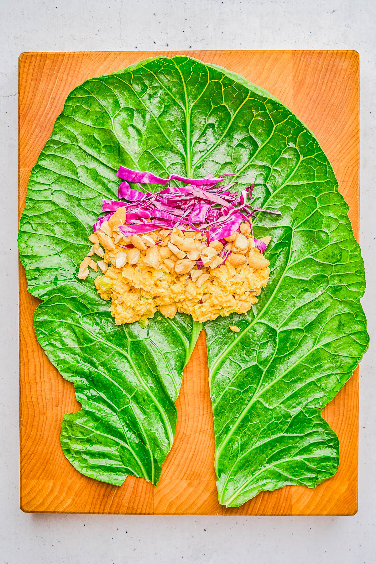 Collard green leaf topped with chickpea mash, shredded purple cabbage, and chopped nuts on a wooden board.