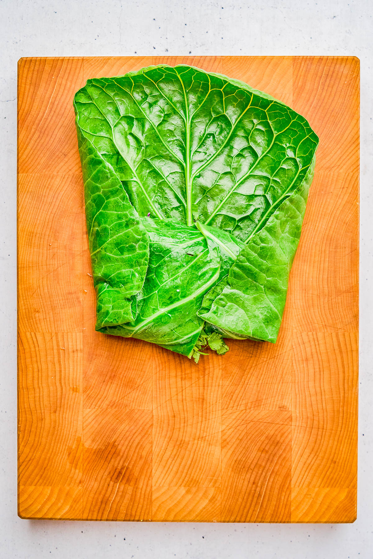 A large green collard leaf folded neatly on a rectangular wooden cutting board.